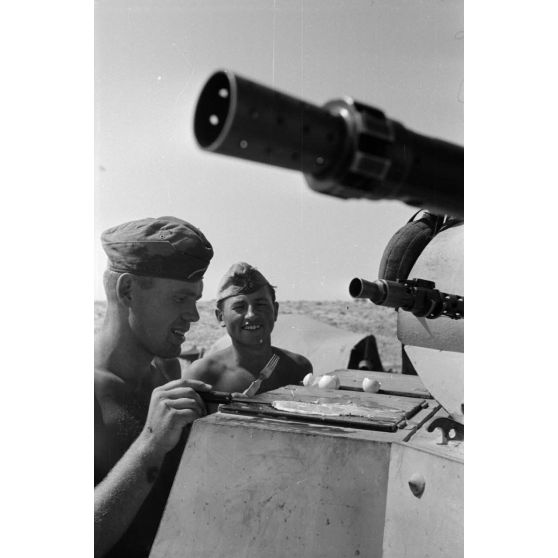 Un homme d'équipage casse des oeufs sur la plaque d'un casier extérieur du Panzer II et les fait cuire.