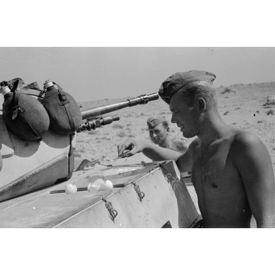 Un homme d'équipage casse des oeufs sur la plaque d'un casier extérieur du Panzer II et les fait cuire.