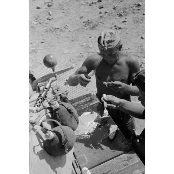 Un homme d'équipage casse des oeufs sur la plaque d'un casier extérieur du Panzer II et les fait cuire.