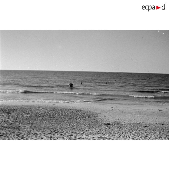 La plage et des baigneurs à proximité d'un camp de prisonniers.