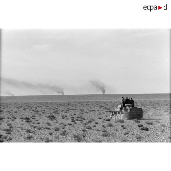 Des chars Panzer III (Pz-III) du Panzer.Regiment 8 (Pz.Rgt-8) progressent dans le désert au milieu de véhicules en flamme.