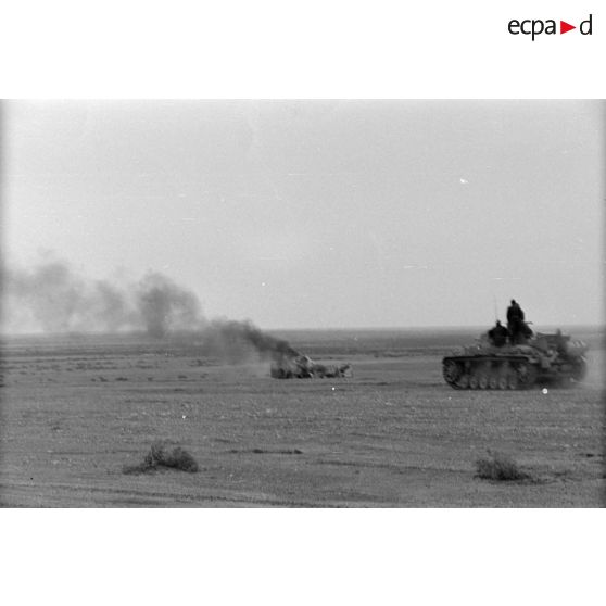 Un blindé allemand Panzer III (Pz-III) passe près d'un véhicule en flamme.