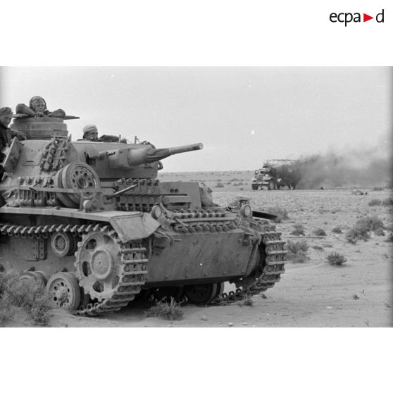 Un Panzer III (Pz-III) passe près d'un camion en flamme.