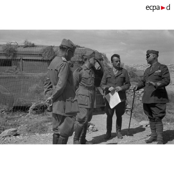 Des officiers supérieurs italiens discutent près d'un bus camouflé sous un filet.