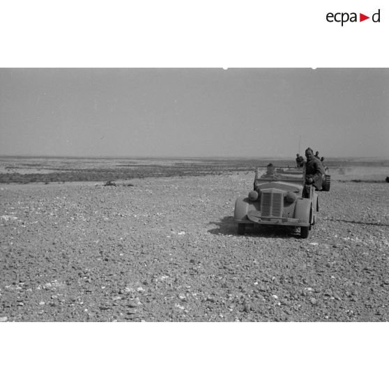 Une colonne de véhicules, dont des voitures et des véhicules blindés, avance dans le sable en soulevant des nuages de poussière.