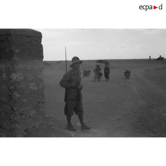 Une sentinelle, baïonnette au canon, à l'arrière-plan des motos et des soldats italiens.