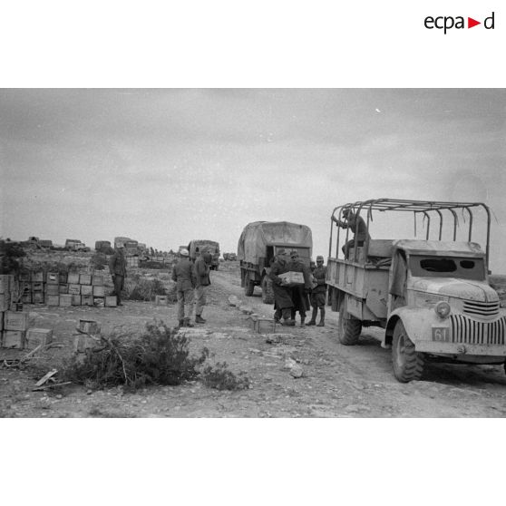 Une colonne de camions composée de camions Opel Blitz et Chevrolet, près des parcs d'approvisionnement, des soldats qui y assurent la manutention.