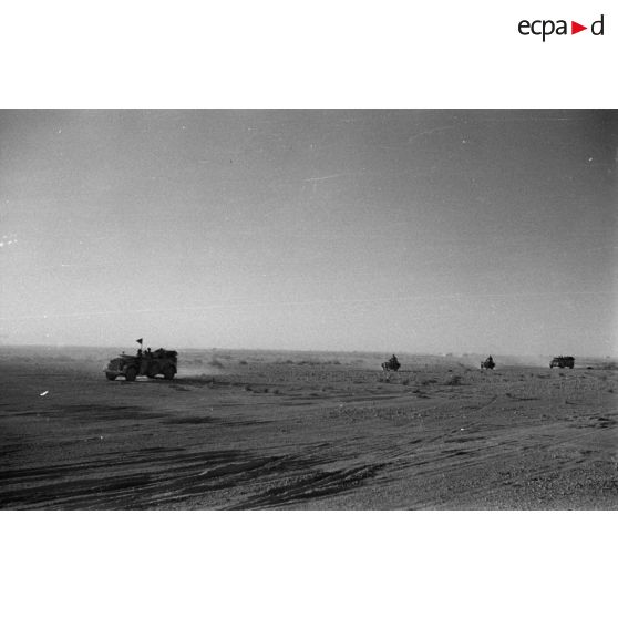Des voitures Kfz-15 suivies de side-cars roulent dans le désert, l'une des voitures porte un fanion.