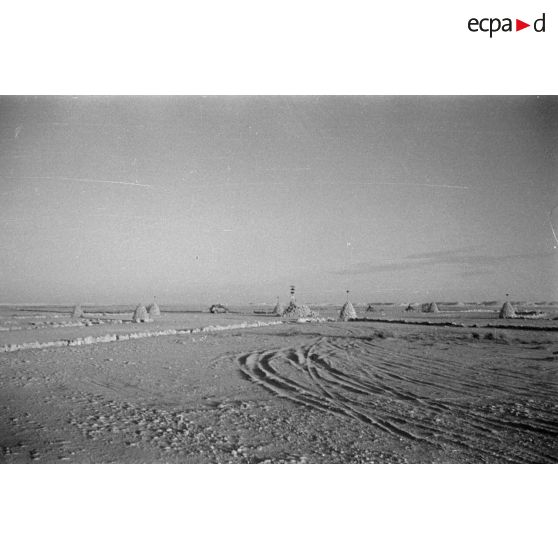 Une voiture Kübelwagen passe au milieu de puits protégés par des constructions en pierre.