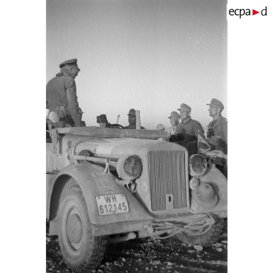 Un officier debout dans une voiture Kfz-12 parle avec des soldats.