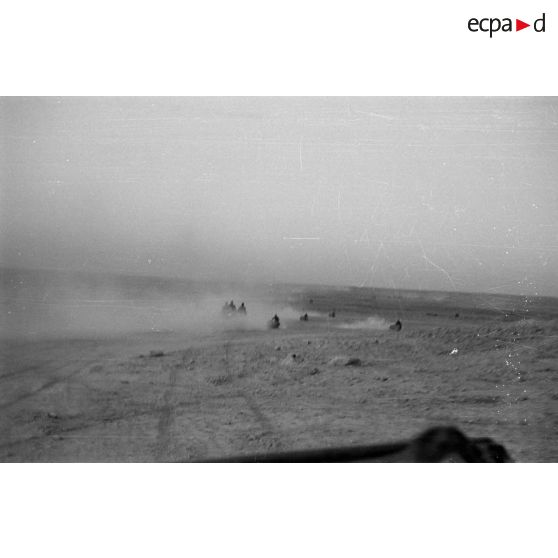 Des véhicules roulent dans le désert en direction d'un secteur de collines.