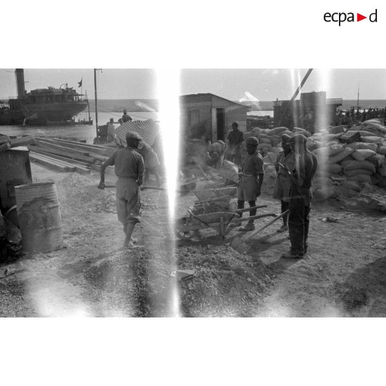 Dans le port de Tobrouk, des ouvriers et des prisonniers britanniques s'activent à la reconstruction des quais.