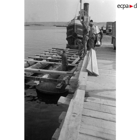 Sur les quais du port de Tobrouk, la construction d'une barge et au second plan le bâteau de pêche Cornelis II.