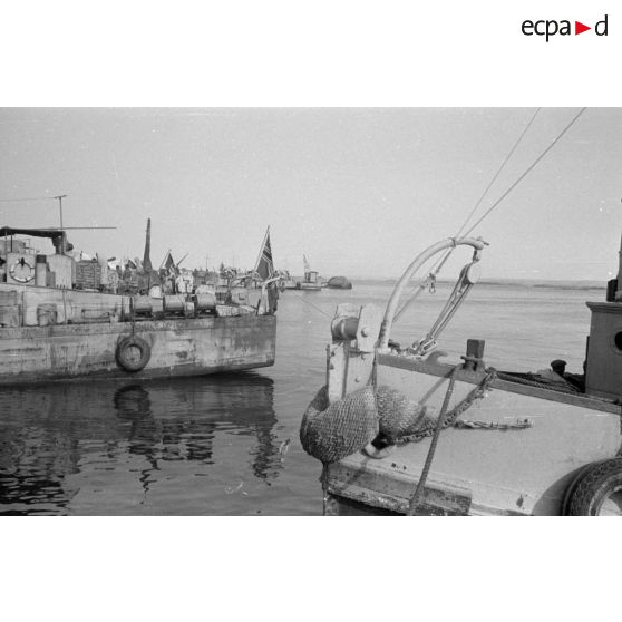 Des navires à quai, aux couleurs italiennes et allemandes, derrière les ruines autour de la rade.