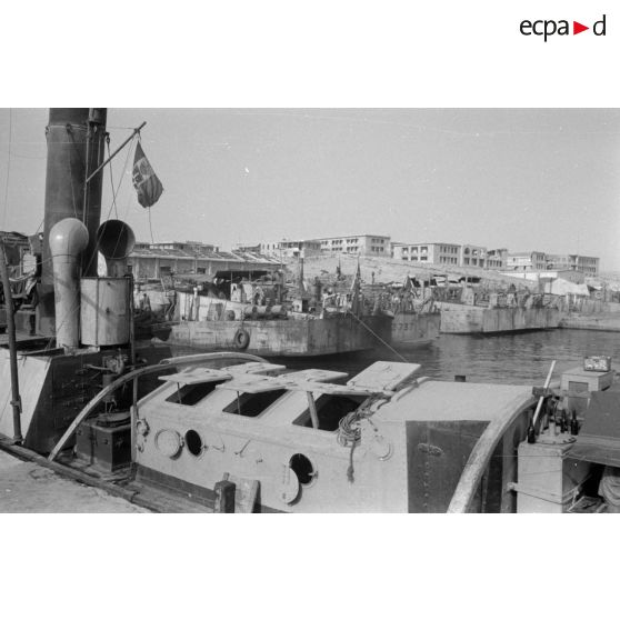 Des navires à quai, aux couleurs italiennes et allemandes, derrière les ruines autour de la rade.