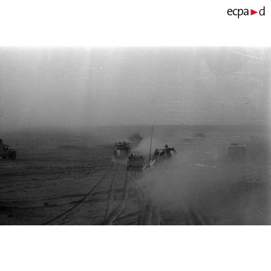 Une colonne de véhicules progresse dans le désert en produisant d'importants nuages de poussière.