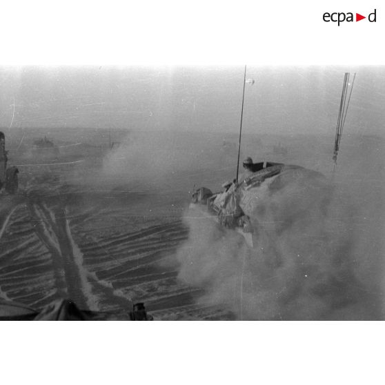 Une colonne de véhicules progresse dans le désert en produisant d'importants nuages de poussière.