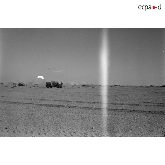 Derrière des traces de pneus et de chenilles marquant une piste, une voiture Kfz-18 et un blindé SdKfz-250.