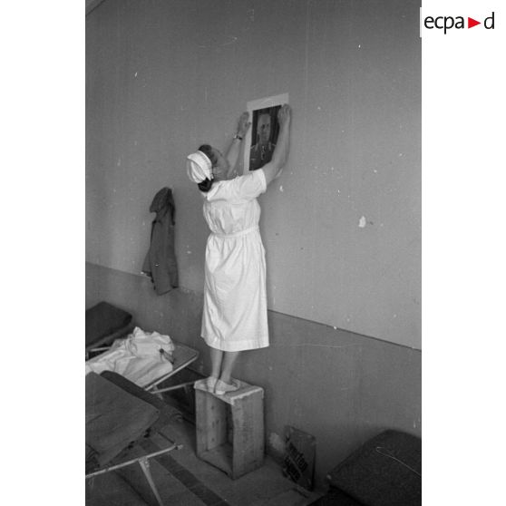 Une infirmière accroche un portrait de Rommel au mur d'une salle de l'hôpital allemand.