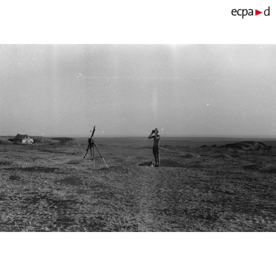 Un soldat observe le terrain à la jumelle près d'une mitrailleuse MG-34 sur trépied.