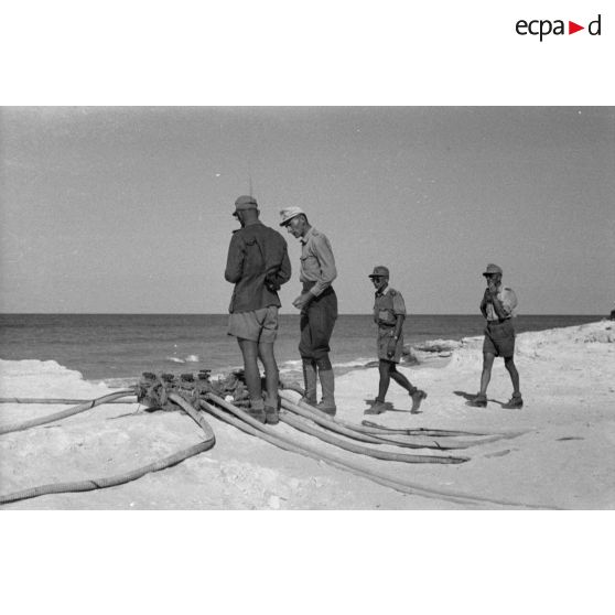 Un groupe d'officiers et de sous-officiers près des tuyaux sur la plage.
