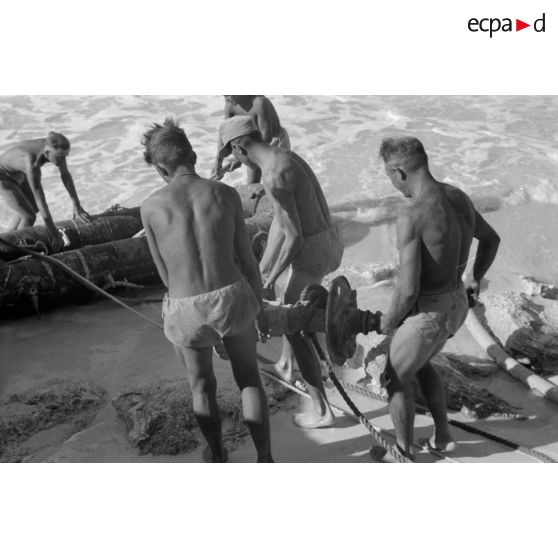 En vue de la désalinisation de l'eau de mer, transport du lest d'un des tuyaux sur un canot pneumatique.