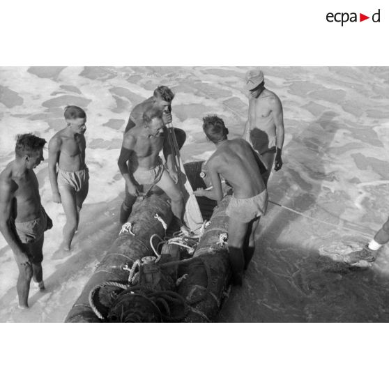 En vue de la désalinisation de l'eau de mer, transport du lest d'un des tuyaux sur un canot pneumatique.