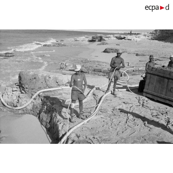 En vue de la désalinisation de l'eau de mer, transport du lest d'un des tuyaux sur un canot pneumatique.