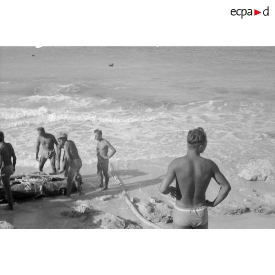 En vue de la désalinisation de l'eau de mer, transport du lest d'un des tuyaux sur un canot pneumatique.