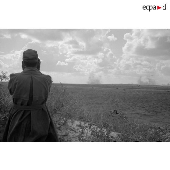 Le groupe d'officiers observe à la jumelle les combats. Impacts d'artillerie dans le désert.