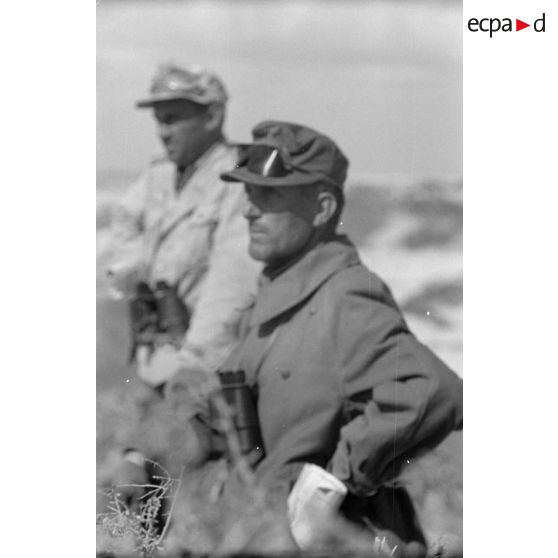 Le groupe d'officiers observe à la jumelle les combats. Impacts d'artillerie dans le désert (image floue).