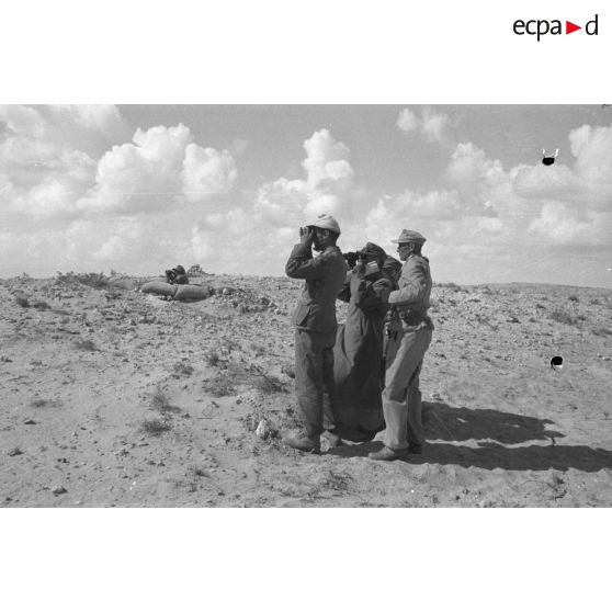 Le groupe d'officiers observe à la jumelle les combats. Impacts d'artillerie dans le désert.
