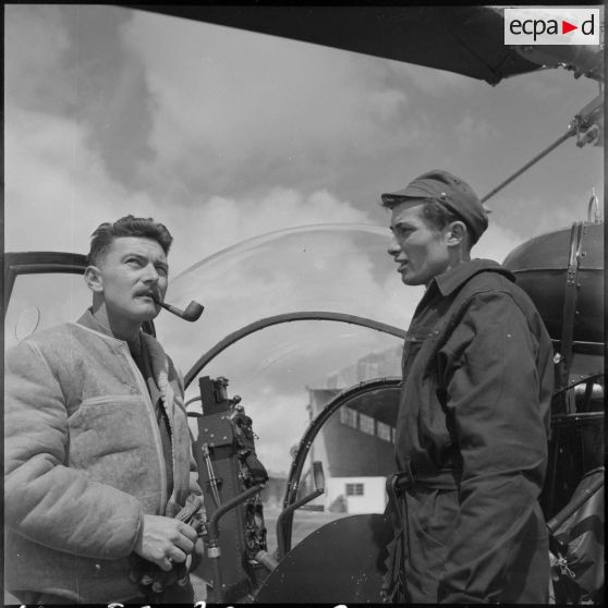 Conversation entre un officier pilote et un mécanicien du groupe hélicoptère n°2 (GH n°2) devant un hélicoptère Bell 47G sur la base d'Aïn Arfat.