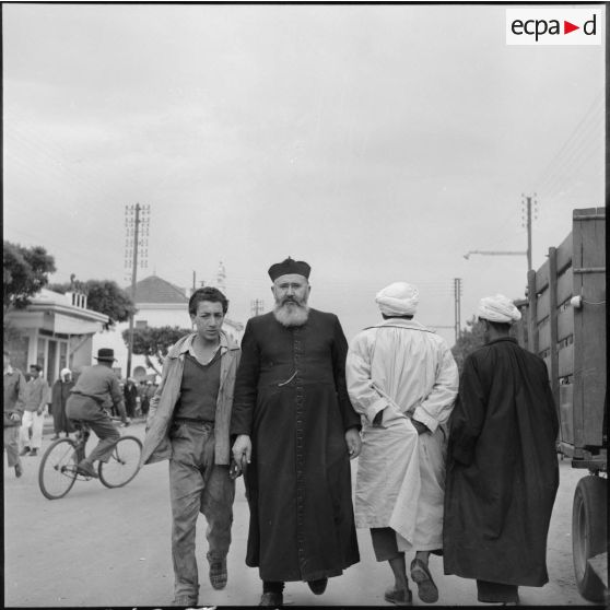 Conversation entre le curé de Morris et un jeune algérien dans les rues du souk.