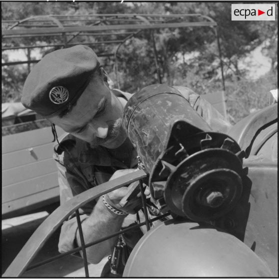 Réparation d'un condensateur à l'avant d'un véhicule GMC par un soldat du 1e REP (régiment étranger de parachutistes) aux environs de Beni-Saf.