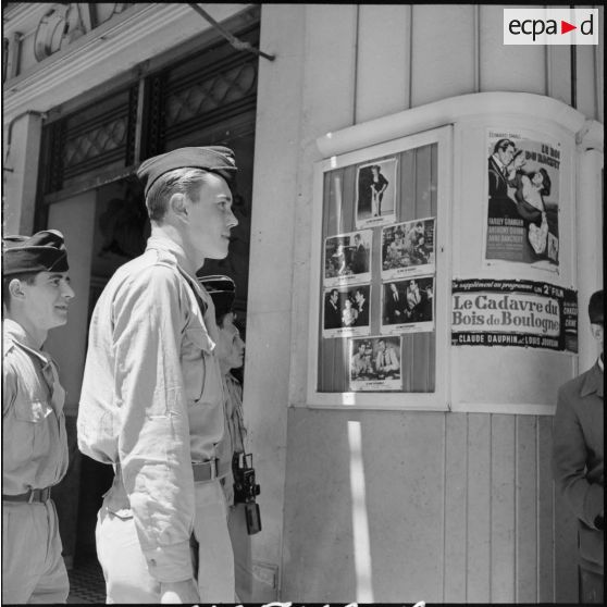 Rappelés en permission à Alger regardant les affiches de films en salle devant un cinéma de la ville.