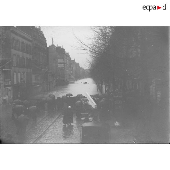 [Piétons attendant au bord de l'eau dans une rue de Paris submergée par la crue.]
