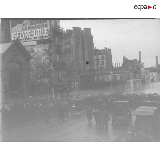 [Piétons attendant au bord de l'eau dans une rue de Paris submergée par la crue.]