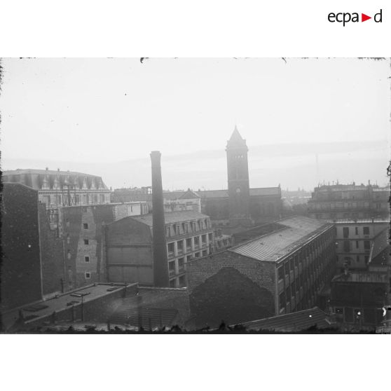 [Vue sur une usine parisienne depuis les toits. Au loin, on aperçoit la tour Eiffel.]