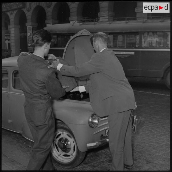 Un lieutenant déposant ses bagages dans le coffre d'une voiture Citroën 4CV.