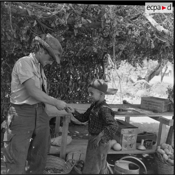 Un soldat d'un régiment d'infanterie achètant du raisin à un jeune commerçant au marché de Loudalouz.