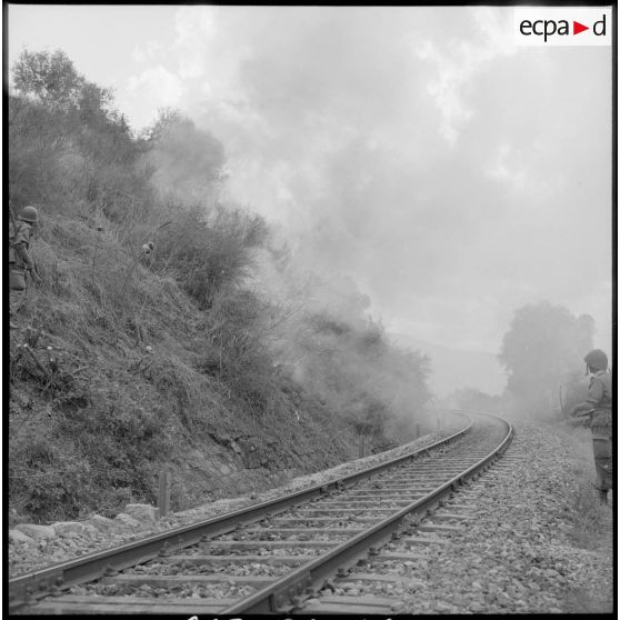 Deux soldats observent la progression d'un incendie volontaire aux abords des voies de chemin de fer.