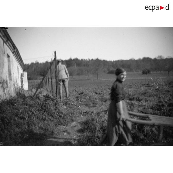 [Jeune femme passant dans un champ dans lequel se promène un soldat, s.d.]