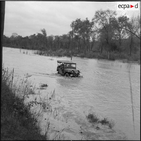 Des soldats en jeep remontent une route inondée près de Bône, le jour de la visite du secrétaire d'état Max Lejeune et du général Salan.