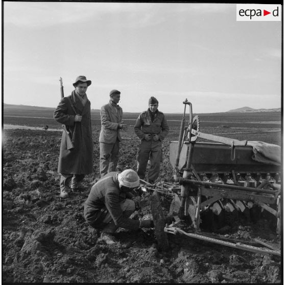 Un paysan algérien répare un tracteur sous le regard de soldats du 9e régiment de tirailleurs algériens (BTA) en mission de protection des activités agricoles près d'Aumale (actuelle wilaya de Médéa).