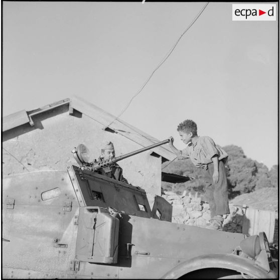 	Un enfant algérien joue avec la mitrailleuse d’une voiture blindée à Aïn Terzine (secteur d’Aumale).