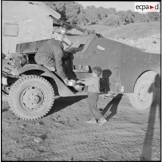Scène de jeu entre un enfant algérien et un soldat du 5e bataillon de tirailleurs algériens (5e BTA) sur sa voiture blindée à Aïn Terzine.