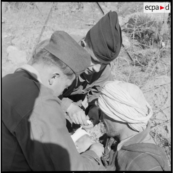 Deux soldats soignent un blessé algérien lors d'une séance d'action psychologique organisée près d'un poste de contrôle militaire.