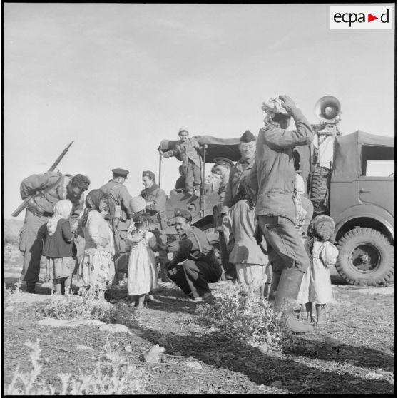 Rencontre entre un groupe d'enfants algériens et des soldats devant le camion d'une compagnie de haut-parleurs et de tracts (CHPT) dans un village.