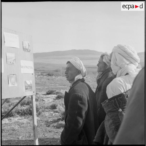 Un groupe d'hommes algériens devant un panneau photographique présenté par une compagnie de haut-parleurs et de tracts (CHPT).